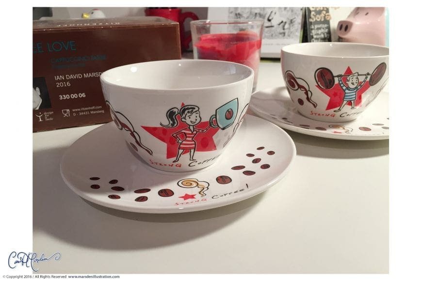 Two ceramic cups with cartoon designs and "Strong Coffee" text, cappuccino package behind.