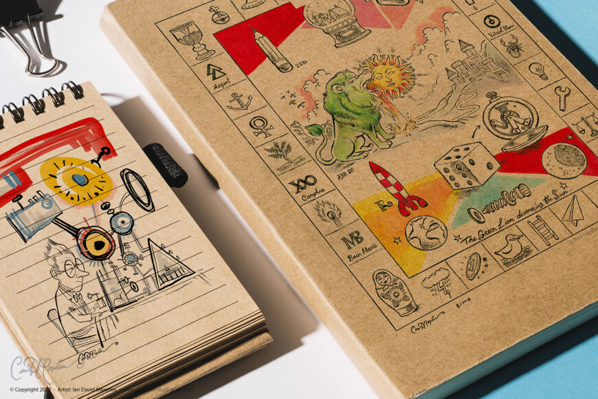 Close-up photo of a sketchbook with colorful surreal illustrations printed on the cover, including alchemical symbols and creatures.