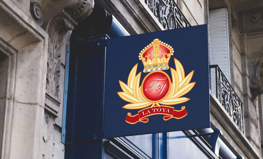 Sign with crown, laurel leaves, "Toy" emblem, "La Toya" ribbon on ornate building exterior.
