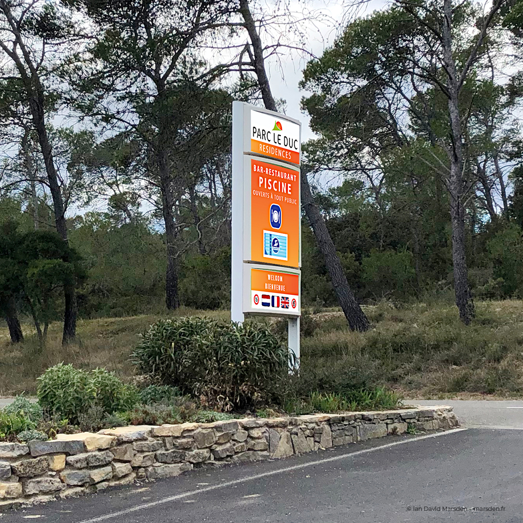 Orange entrance signage to Parc area with pool and restaurant symbols on freestanding totem