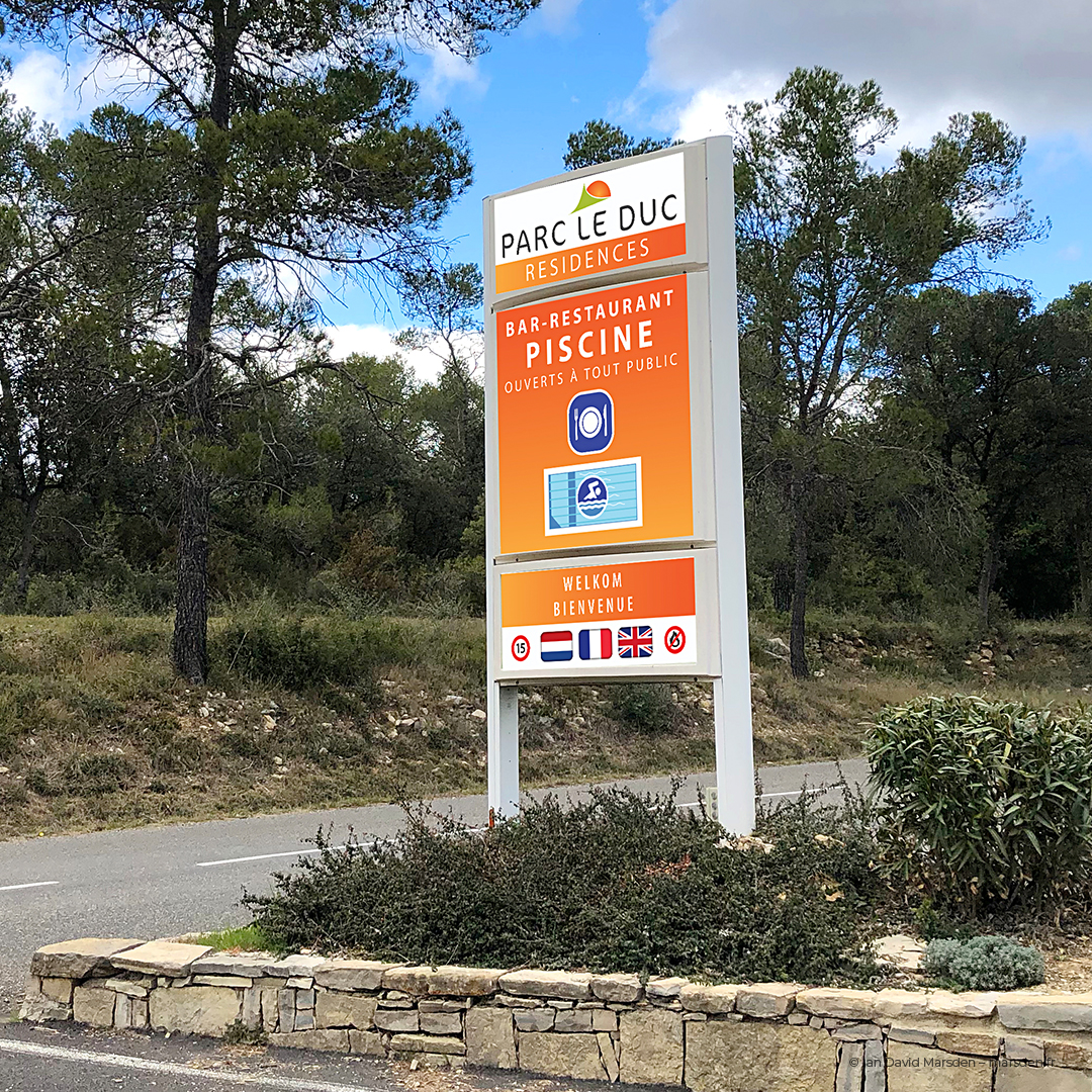 Full-height view of branded orange totem sign for entrance area with pool and café icons