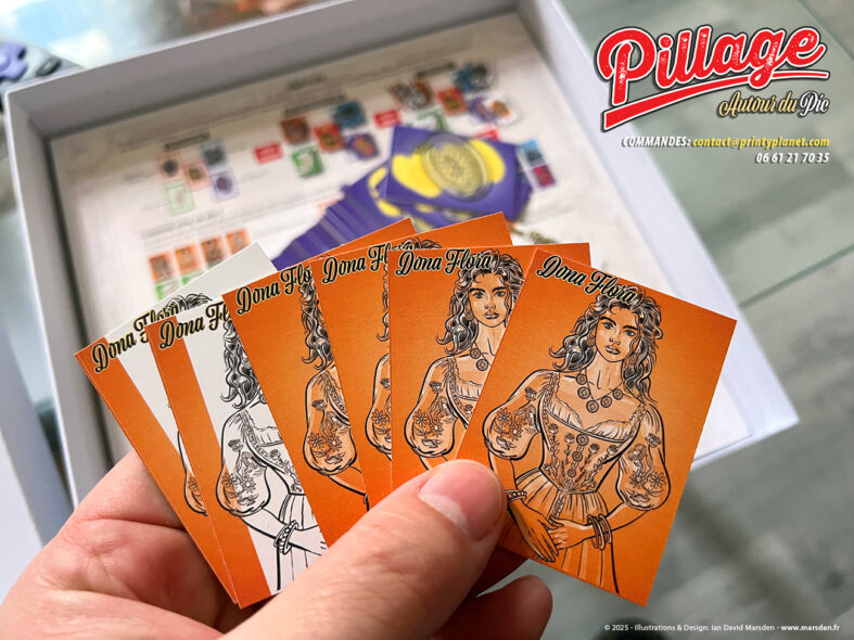 Cartes de personnage Dona Flora du jeu Pillage autour du Pic tenues en main, avec boîte et plateau visibles en arrière-plan.