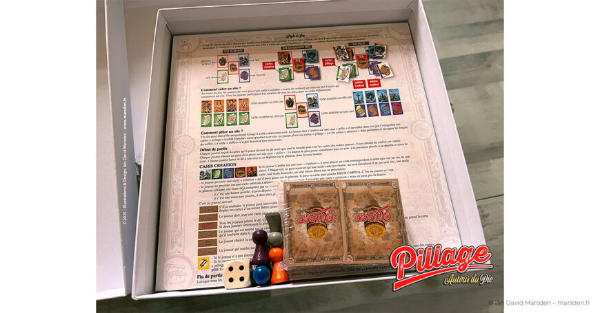 Intérieur de la boîte de Pillage autour du Pic avec règles imprimées, cartes, pions, dé et éléments de jeu.