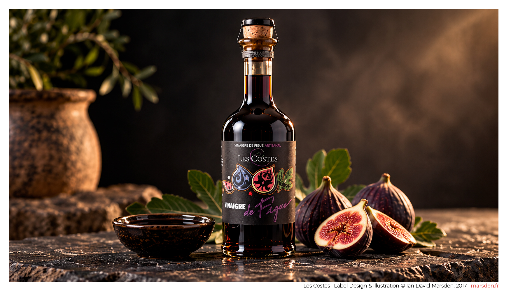 Dark glass fig vinegar bottle with colorful illustrated figs and decorative typography designed by Ian David Marsden, displayed beside fresh figs and a ceramic dish.