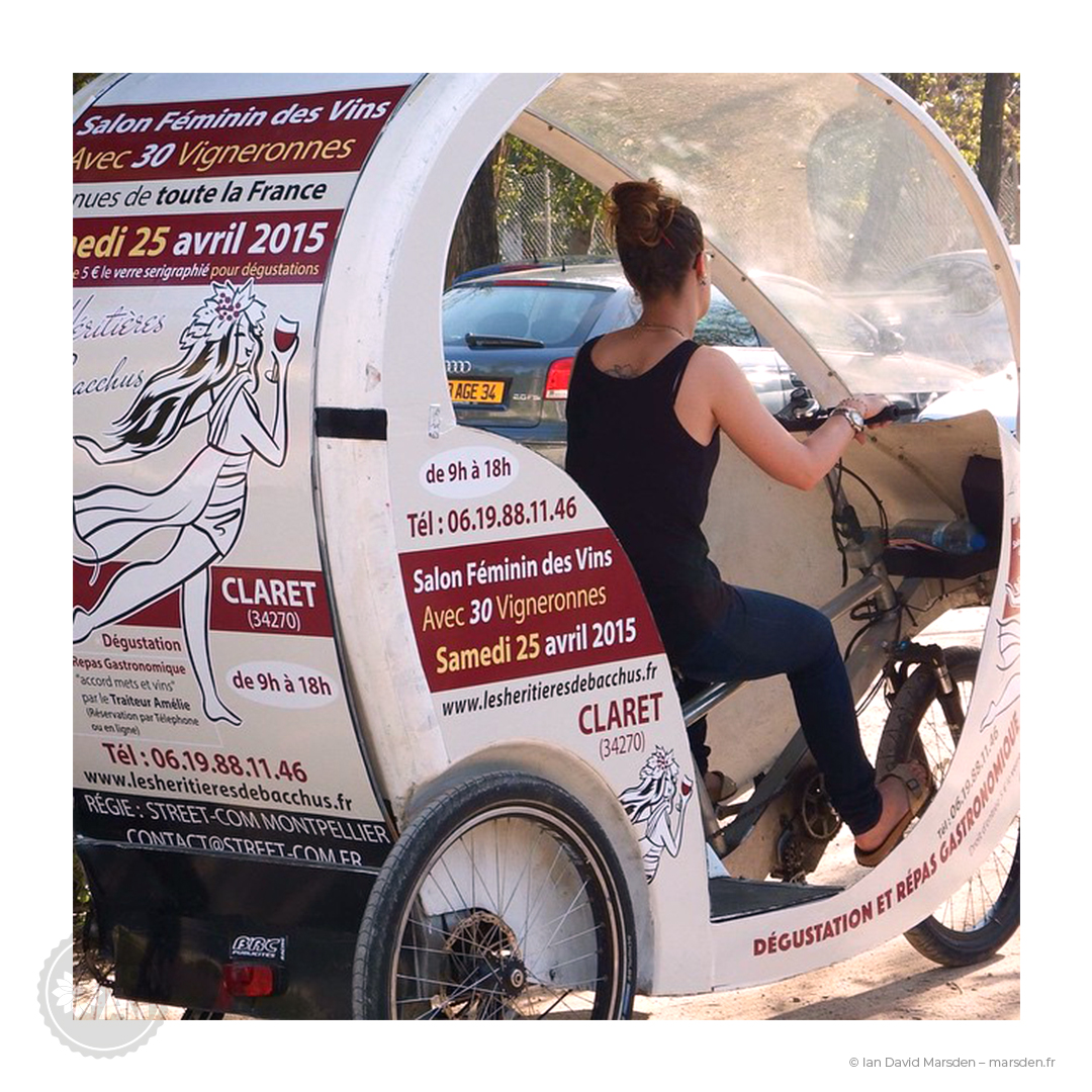 Vue rapprochée du côté d’un vélo-taxi avec le logo illustré Les Héritières de Bacchus et les informations du salon 2015 imprimées sur la carrosserie.
