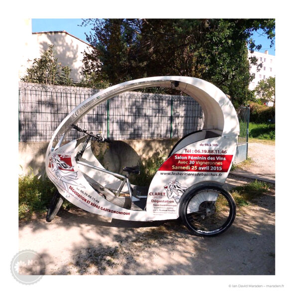 Vue latérale complète du vélo-taxi blanc personnalisé pour Les Héritières de Bacchus, stationné en extérieur et recouvert des adhésifs du salon 2015.