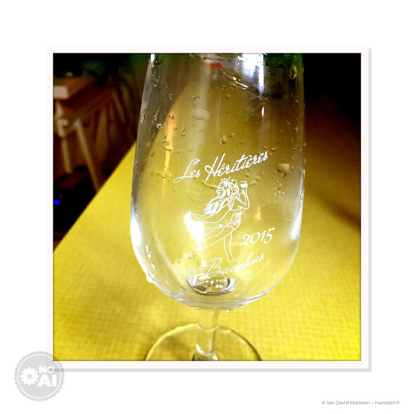 Gros plan d’un verre de dégustation avec la silhouette féminine et le lettrage Les Héritières de Bacchus 2015 sérigraphiés en blanc.